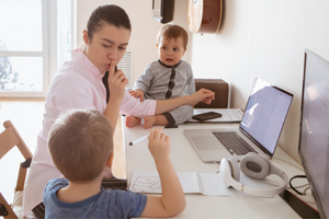 Woman signalling for children to be quiet as she works at her laptop
